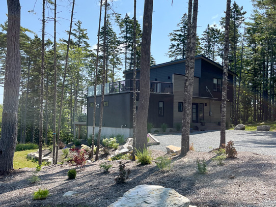 Completed brown two story house with second level deck, on landscaped yard